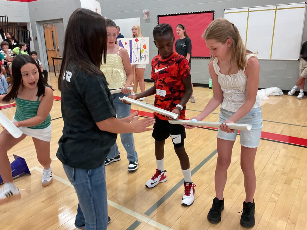 A group of students participate in a team-building activity, holding a long object while focused on each other.
