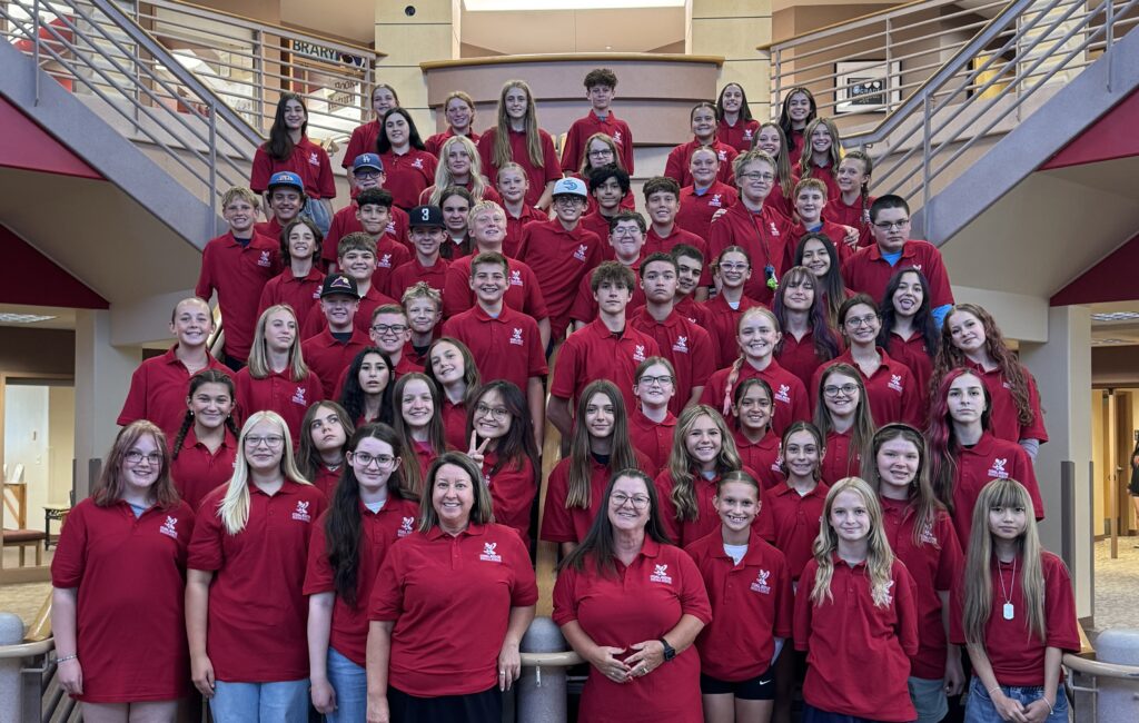 A large group of students and teachers in red shirts poses together on a staircase in a school setting.