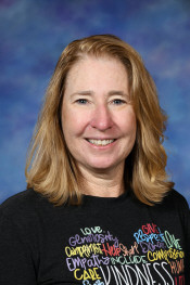 Smiling woman with shoulder-length blonde hair, wearing a black shirt with colorful words about kindness and respect.