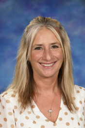 A smiling woman with long blonde hair, wearing a polka dot shirt, against a blue background.