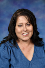 A woman with dark hair smiling, wearing a blue top, against a soft blue and purple background.