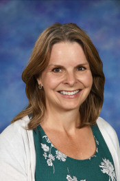 Smiling woman with shoulder-length brown hair, wearing a green floral top and white cardigan, against a blue background.