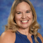 A smiling woman with long, wavy blonde hair, wearing a blue shirt, against a colorful backdrop.