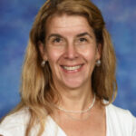 Smiling woman with long, wavy hair wearing a white top, set against a blue background.