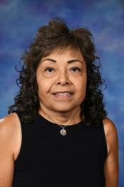 Portrait of a woman with curly hair, wearing a black sleeveless top, set against a blue background.