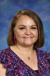 A woman with shoulder-length brown hair smiles, wearing a colorful patterned top and earrings, against a blue background.