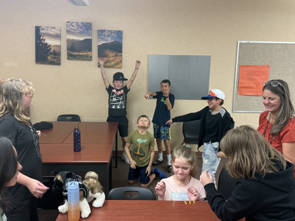 A group of children and adults are engaged in a fun activity in a classroom, with laughter and excitement visible.