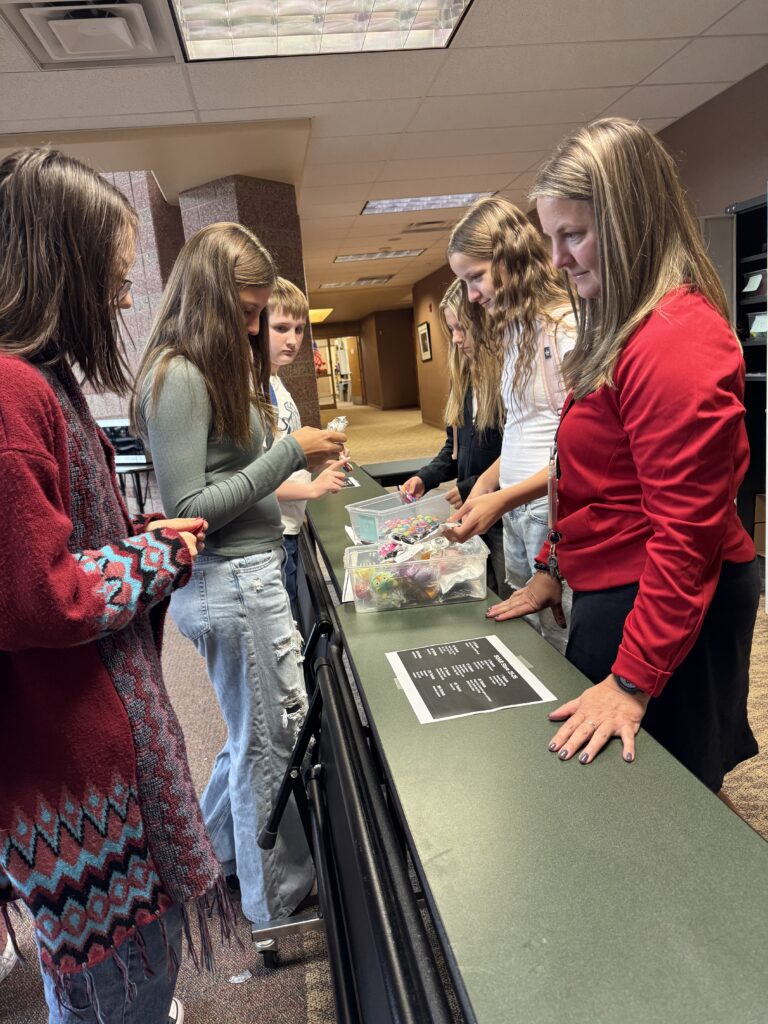 A group of students and a teacher gather around a table, engaging with materials and discussing activities.
