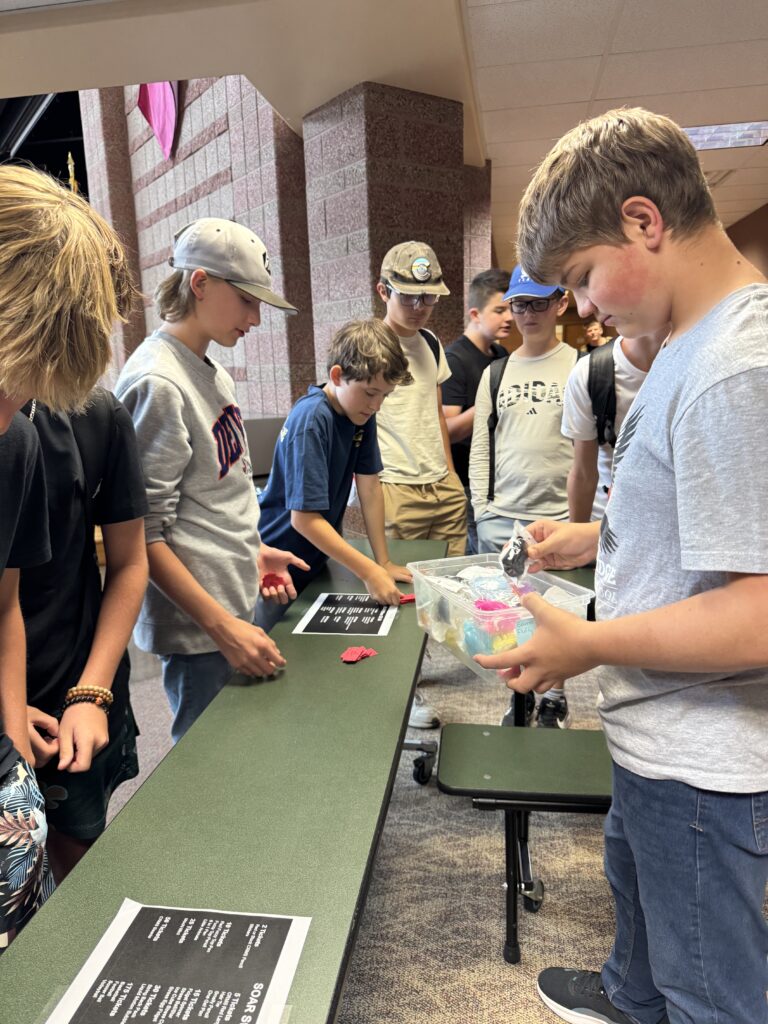 A group of students gathers around a table, examining colorful items in a clear container.