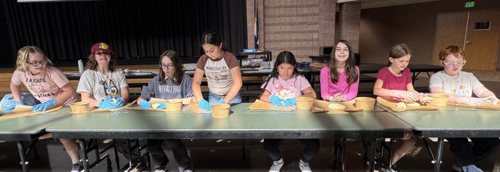 A group of children are sitting at a table, working on a craft project with gloves and materials in front of them.