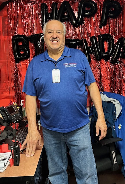A smiling man in a blue shirt stands in front of a "Happy Birthday" banner, surrounded by festive decorations.