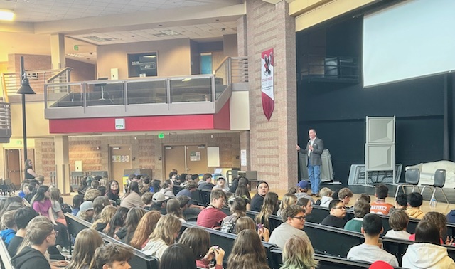 A speaker addresses a large group of students seated in a school auditorium with a modern design.
