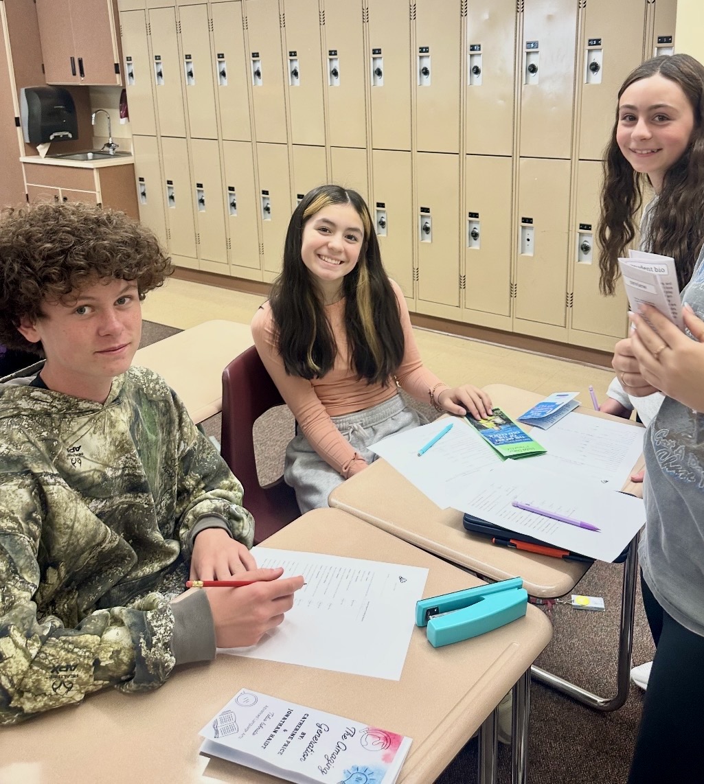 Tres alumnos están sentados en una mesa en un aula, realizando una actividad en grupo con hojas y material.