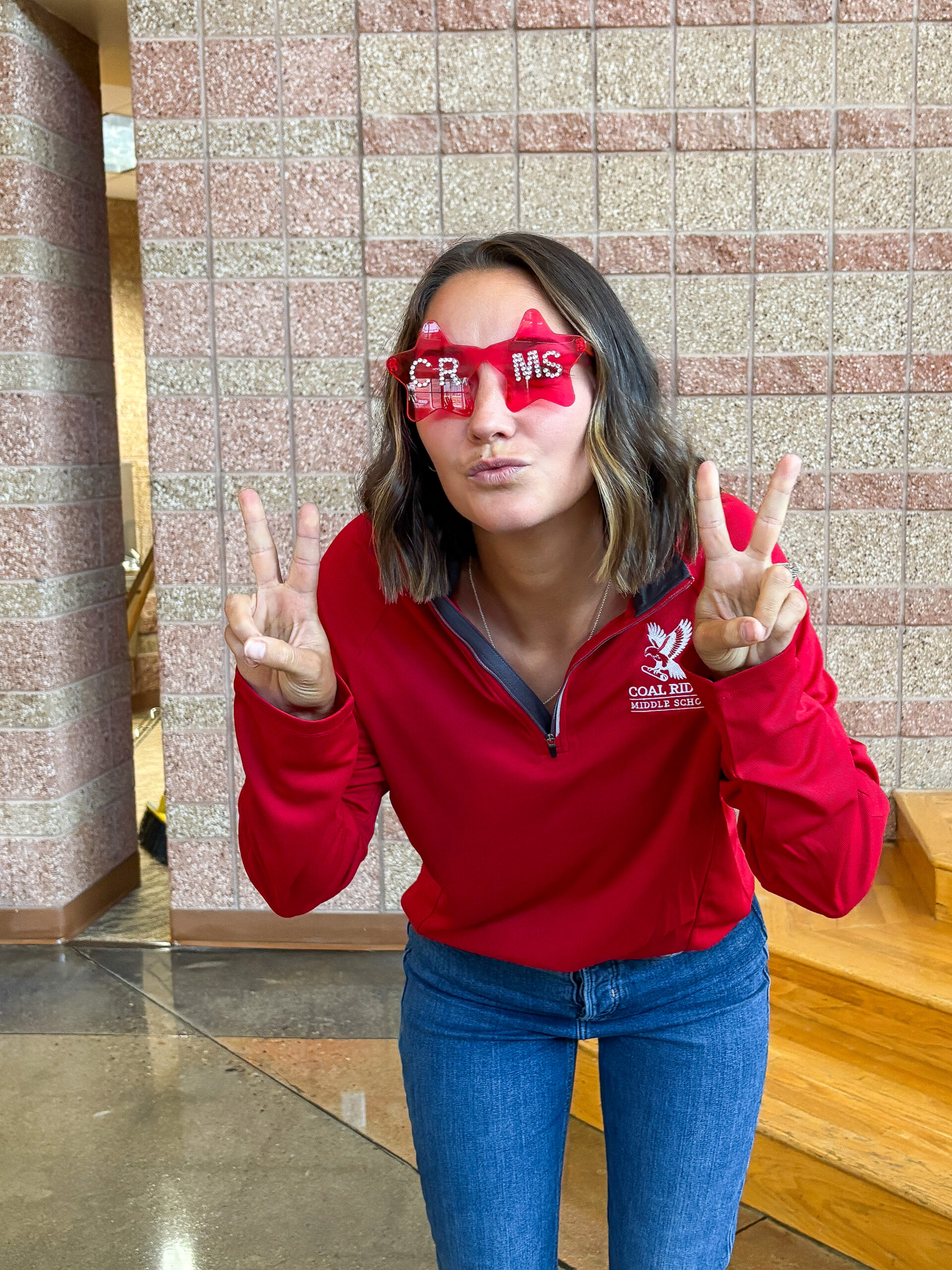 A young woman in a red sweatshirt poses with peace signs, wearing star-shaped glasses that say "CRMS."