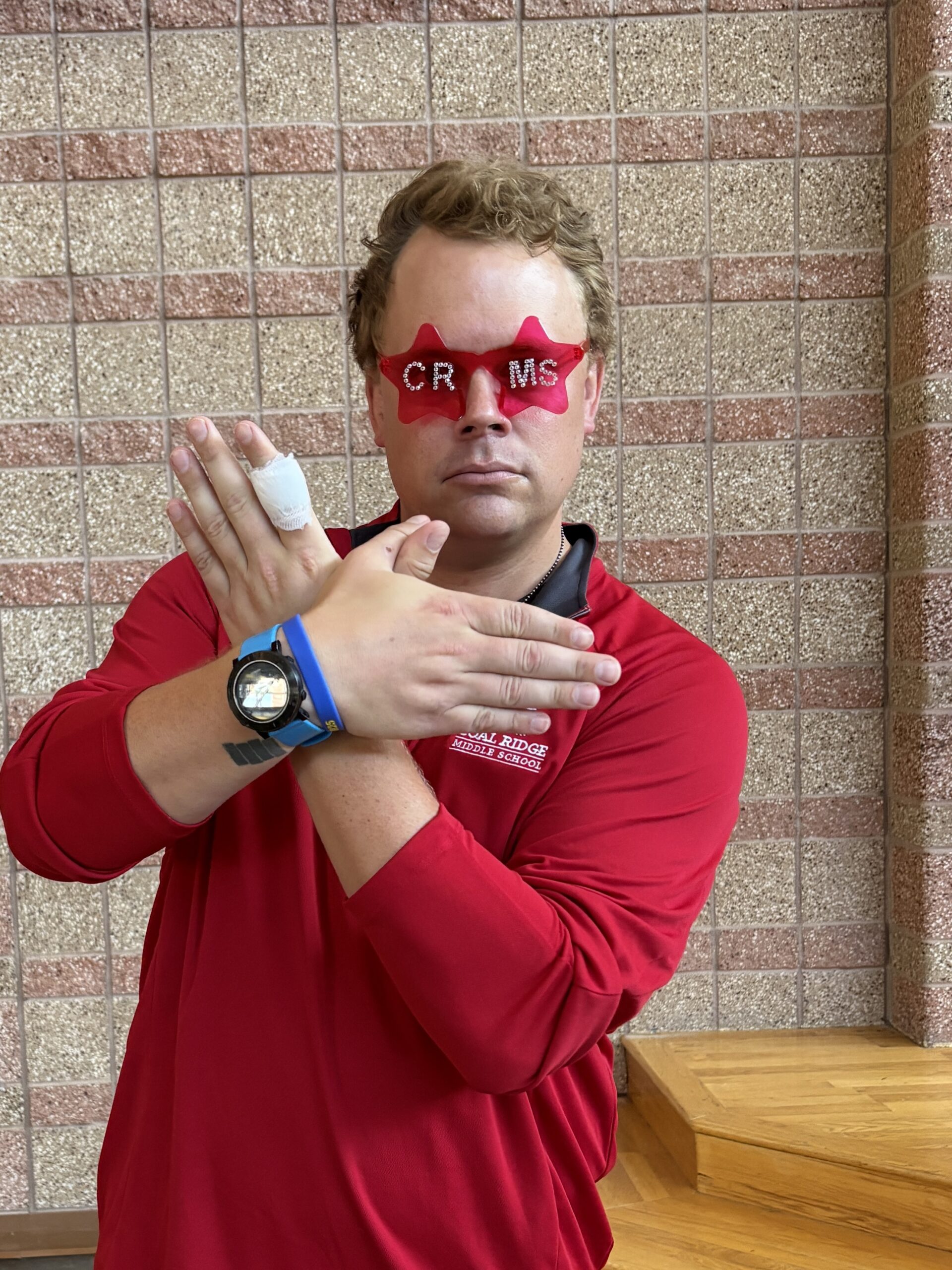 Una persona con una camiseta roja posa con unas gafas en forma de estrella y una mano vendada, mostrando una actitud divertida.